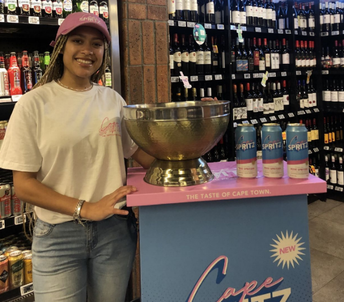 A woman standing next to a bottle of Cape Spritz wine in a store.