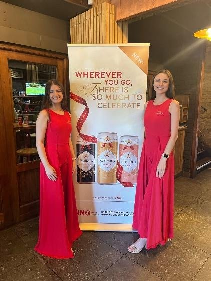 Two women in red dresses standing in front of the latest innovation banner from JC Le Roux.